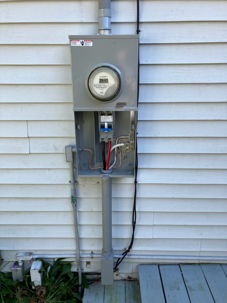 Exterior-mounted electrical panel with visible conduit and wiring, installed by electrical contractors in Cohasset, MA.