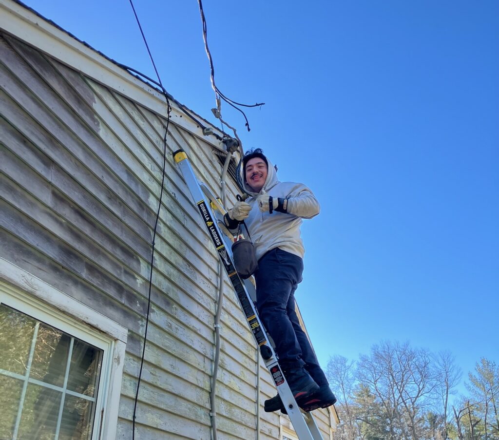 An electrician works on overhead service wires, a common part of Duxbury electrical service upgrades.